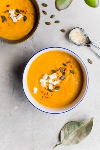 Bowl of healthy butternut squash soup topped with feta cheese, seeds and herbs